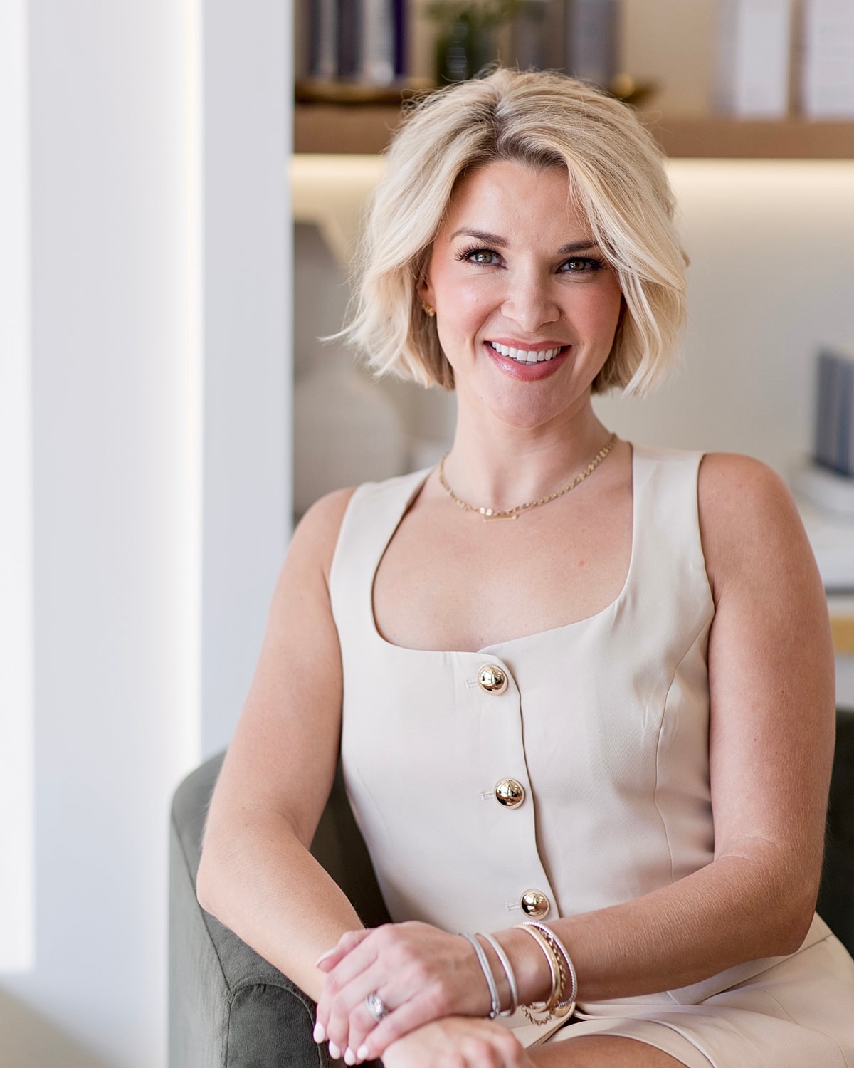 Smiling woman in stylish outfit, seated indoors.