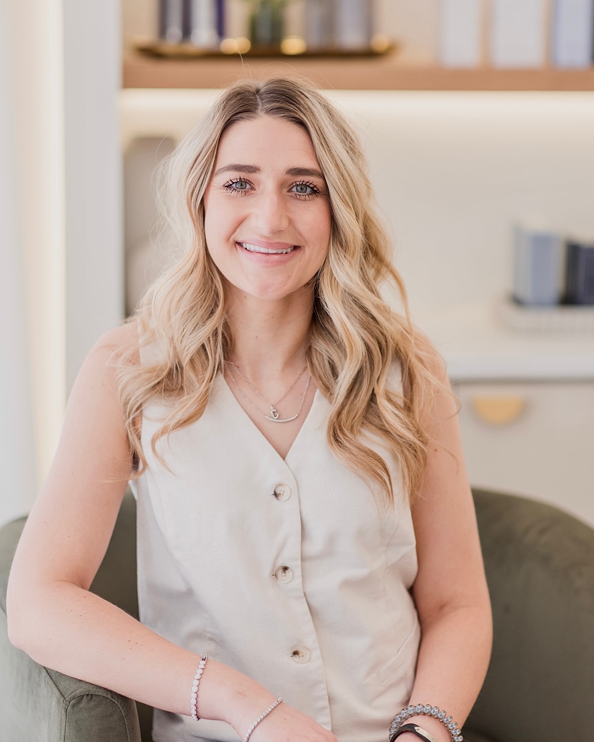 Smiling woman in neutral outfit sitting indoors.