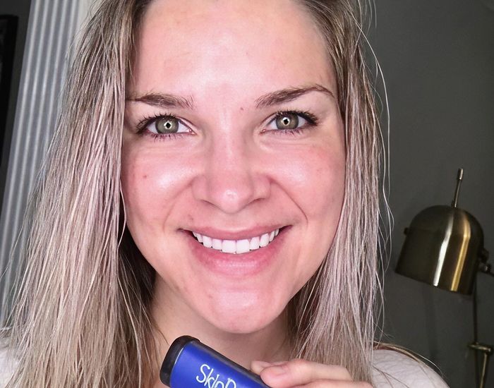 Smiling woman holding a skincare product.